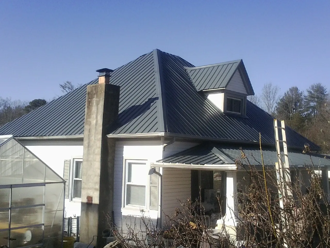 Dark blue standing seam metal roof on a white farmhouse with dormer — Slate & Tile Roof Repair by Roofing Brothers in Hidden Valley