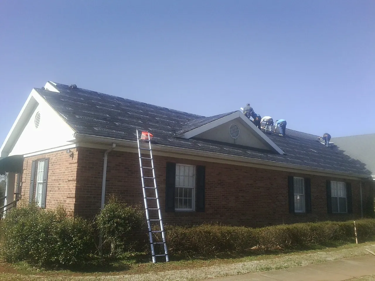 Crew tearing shingles off a brick ranch roof with a ladder set — Metal Roof Repair work by our crew in Hidden Valley