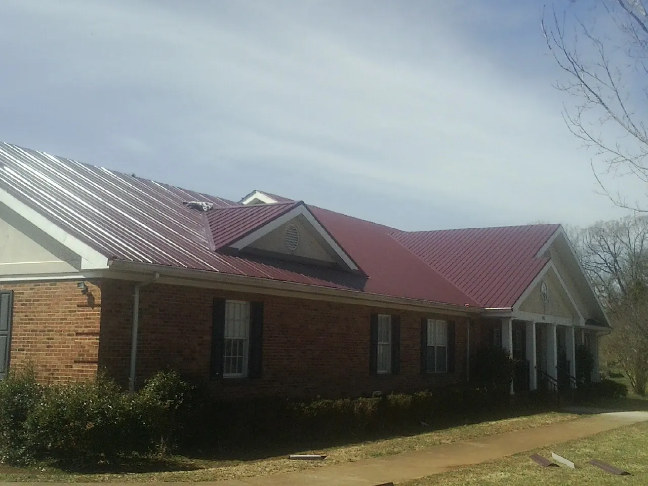 Red metal roof with gabled entries on a long brick building, from a Hail Damage Roof Repair job in Hidden Valley