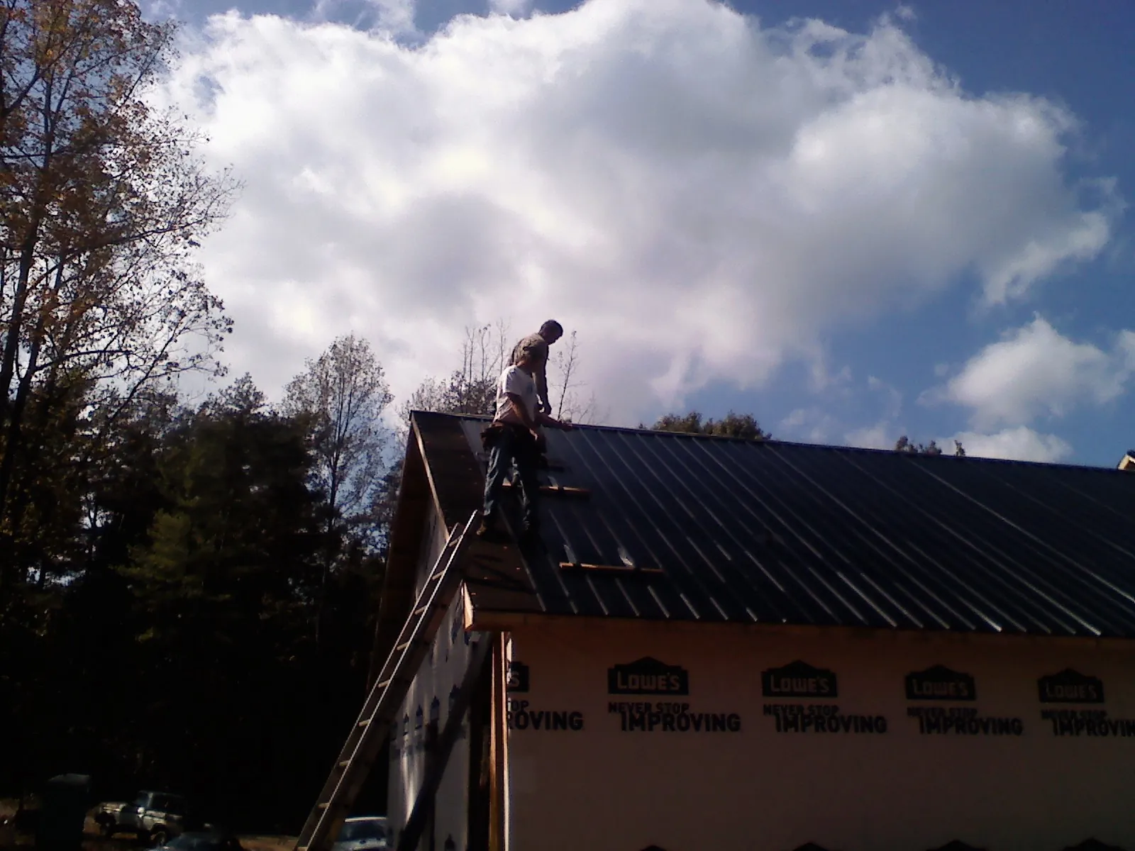 Roofer fastening dark metal panels high against a cloudy sky, from a Roof Inspection job in Hidden Valley