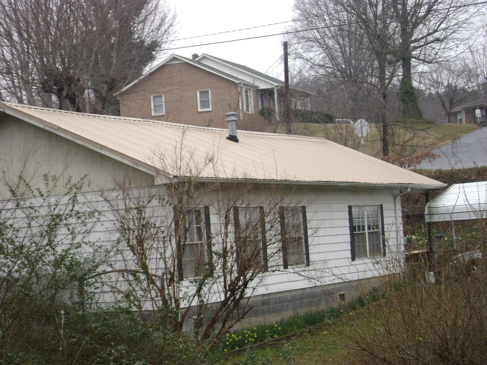 Tan metal roof on a white sided house set into a hillside — Commercial Roofing by Roofing Brothers in Hidden Valley